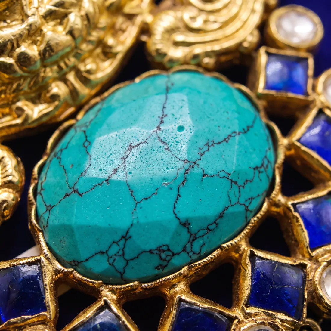 Macro of the faceted turquoise cabochon and blue enamel on a gold temple pendant